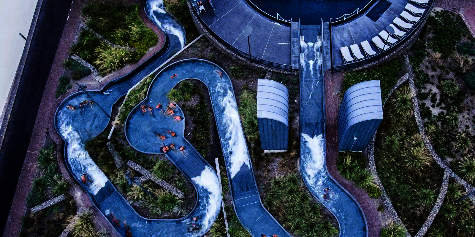 Vogelperspektive auf einen blauen Wildwasserfluss, in dem sich mehrere Personen befinden.