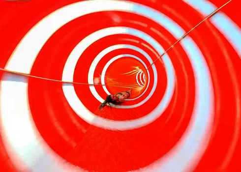 Eine rote Wasserrutsche von innen, mit einer Frau, die rücklings rutscht.