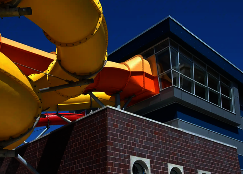 Mehrere bunte Wasserrutschen verlaufen von einem verglasten Gebäudeturm ins Freie.