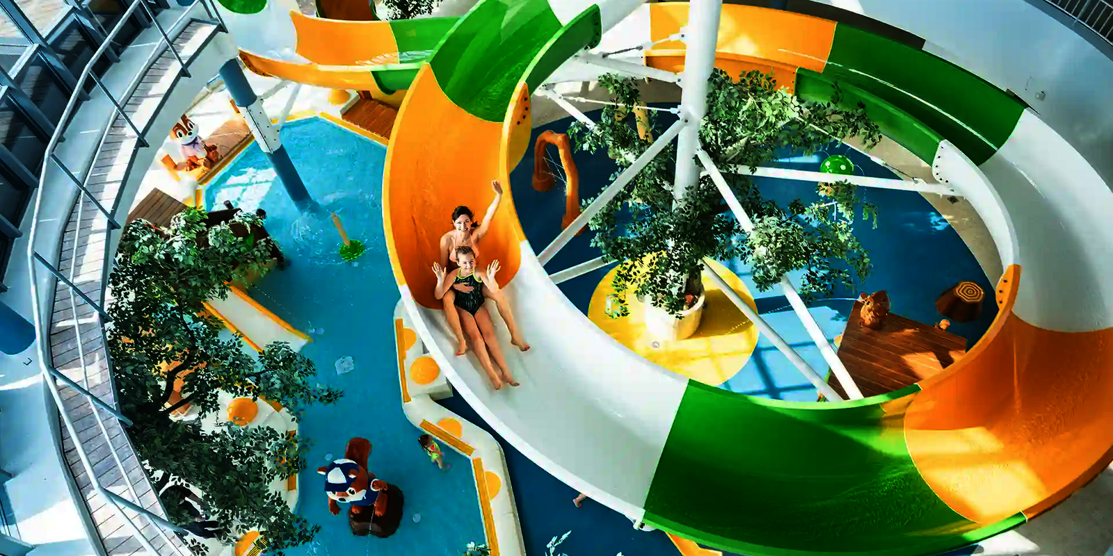 Indoor-Wasserrutsche mit grünen und gelben Elementen, zwei Personen rutschen gemeinsam hinunter