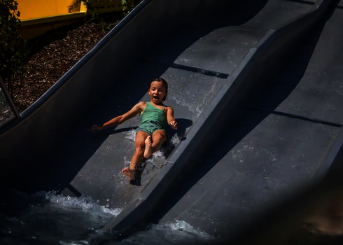 Ein Mädchen rutscht lachend auf der mittleren Bahn der Trio-Slide ins Wasser.