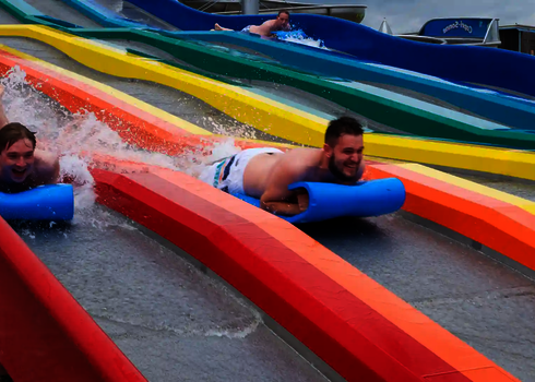 Zwei Personen auf blauen Rutschmatten auf einer bunten Matracer Wasserrutsche.