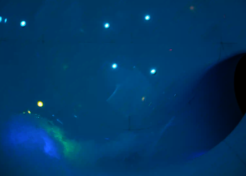 Blaue Innenansicht einer Röhre mit bunten LED-Punkten und Wasserlauf zur Kurve.