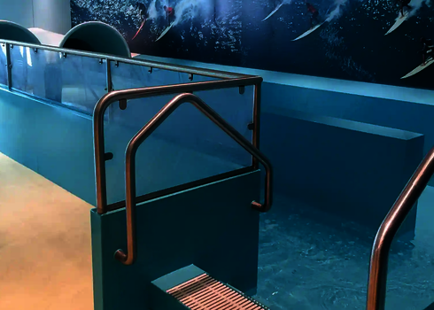 Stainless steel handrail at the slide exit with glass partition and turquoise water.