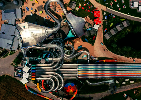 Vogelperspektive des Galaxy Erding Wasserparks mit bunter Rutschenlandschaft und Liegenwiesen.