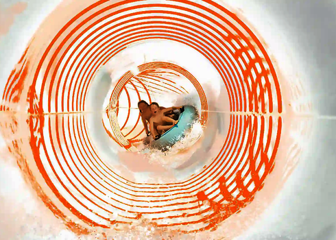 Eine weiße Wasserrutsche von innen, mit zwei Kinder auf einem Rutschreifen und orangenen Lichteffekten..