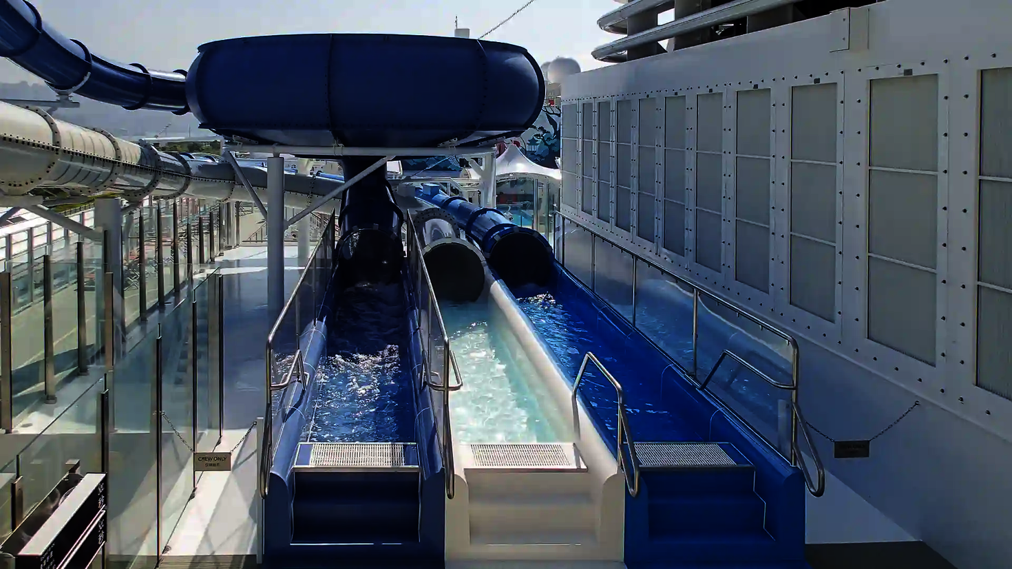Two adjacent slide exits on a cruise ship with a water pool.