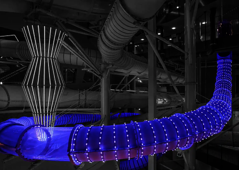 Eine blau beleuchtete Wasserrutsche mit weißen LED-Lichteffekten in einem Hallenbad.