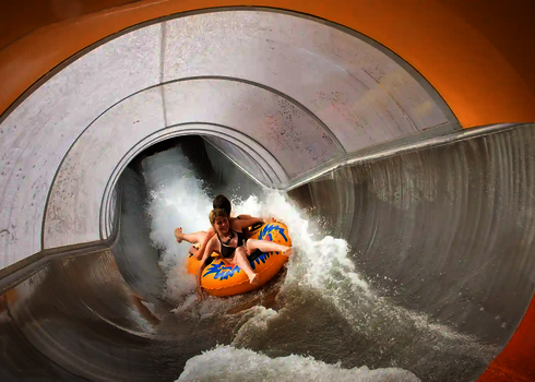 Der Speed Blaster führt zwei Kinder auf einem Doppelreifen durch einen orangenen Rutschabschnitt.