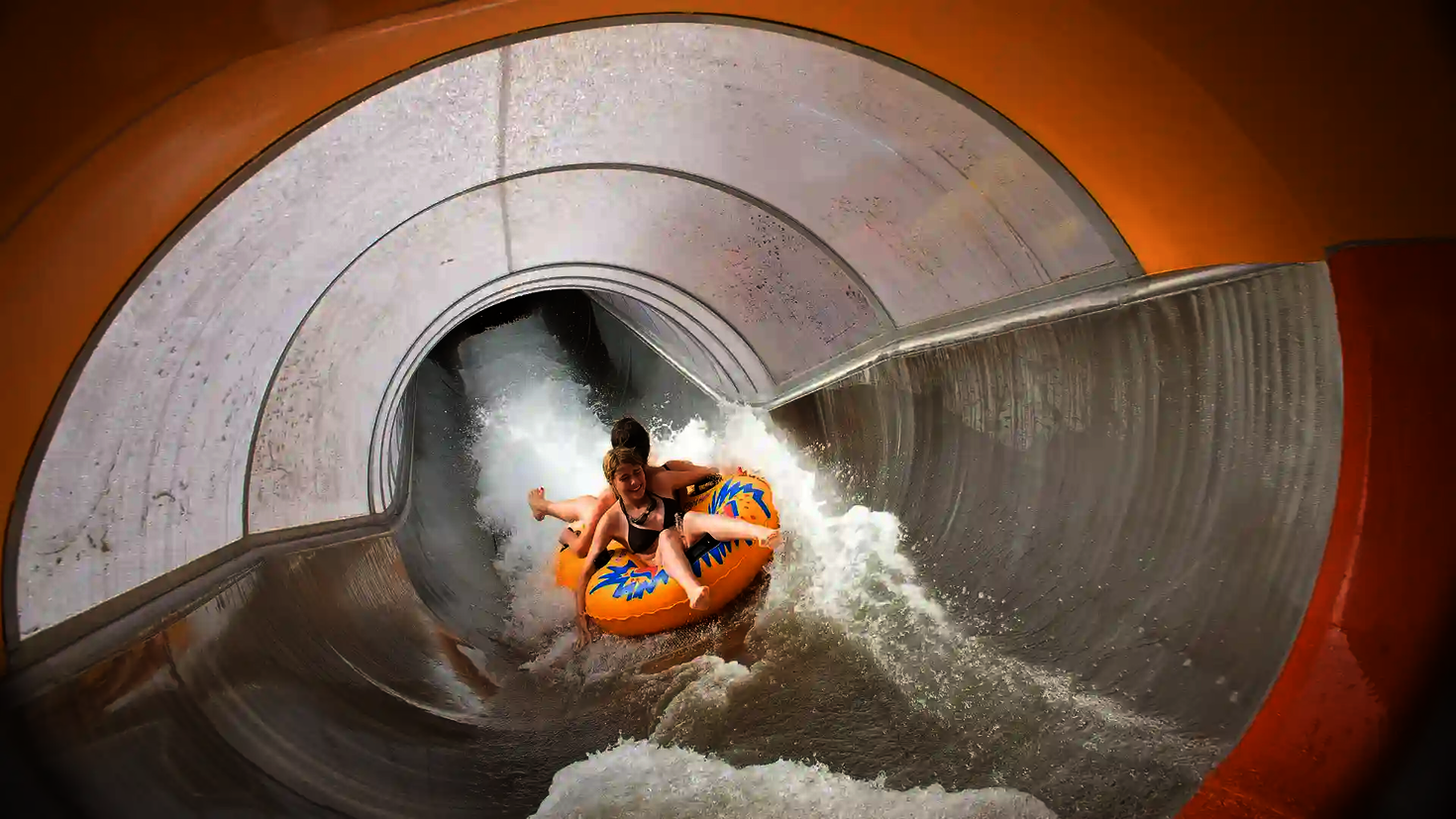 Der Speed Blaster führt zwei Kinder auf einem Doppelreifen durch einen orangenen Rutschabschnitt.