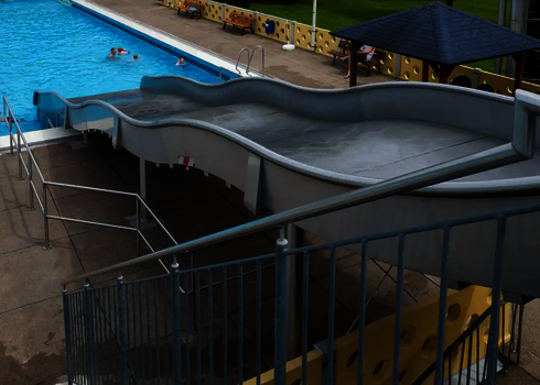 Seitlicher Blick auf eine Breitwellenrutsche, die in ein Schwimmbecken mündet.