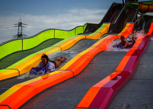 Nahaufnahme von drei Personen auf bunten Matten beim Rutschen auf der Wasserrutsche Matracer.