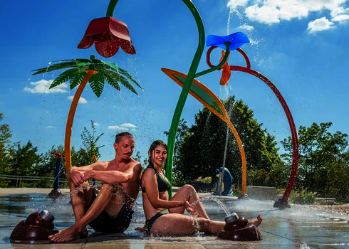 Zwei Personen sitzen lachend auf dem Boden zwischen Wie-Spray Elementen.