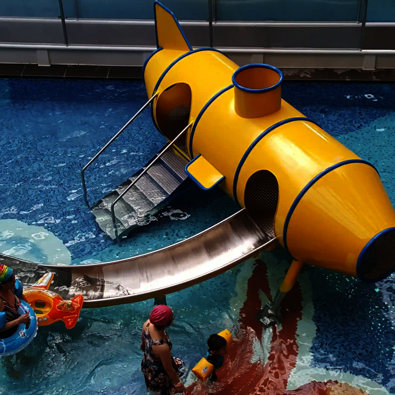 Kinder und Erwachsene befinden sich in einem Kinderbecken mit dem gelben Wie-Spray Element "U-Boot".