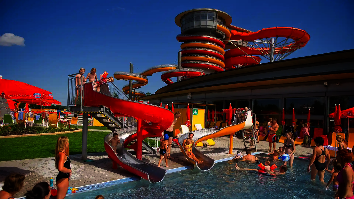 Viele Badegäste sind auf und neben roten und orangenen Wasserrutschen in der Therme Lutzmannsburg.