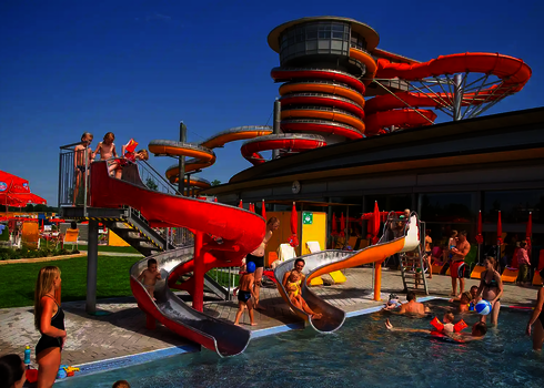 Viele Badegäste sind auf und neben roten und orangenen Wasserrutschen in der Therme Lutzmannsburg.