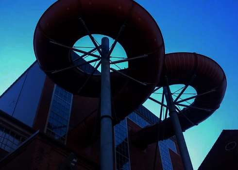 Rote Family Twister Wasserrutsche mit Spiralabfahrt vor Backsteingebäude.