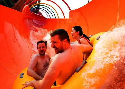 Drei Erwachsene lachen beim Rutschen mit dem gelben Reifen durch den orangenen Tunnel der RR2700.