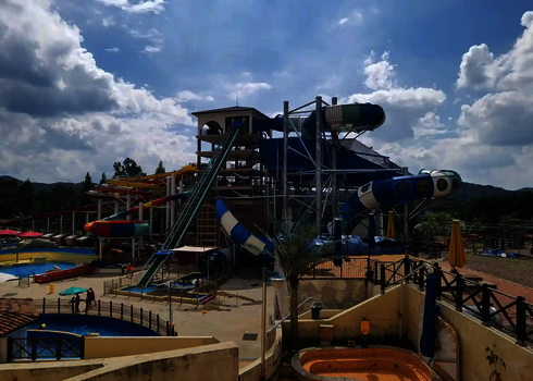 Panorama of a water park with raft conveyor, slide landscape, and spacious pool area.