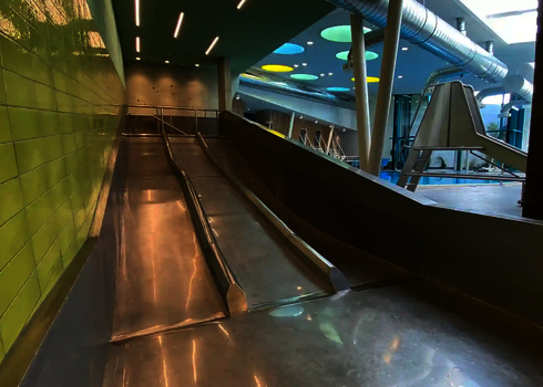 Blick auf die Trio-Slide aus Edelstahl, links grüne Fliesenwand, rechts Badebereich.