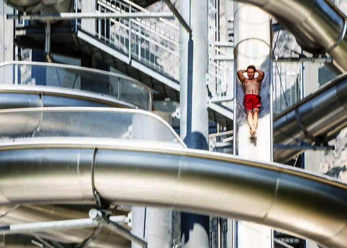 Ein Mann in roter Badehose rutscht in gerader Haltung durch eine steile Freifall-Wasserrutsche.