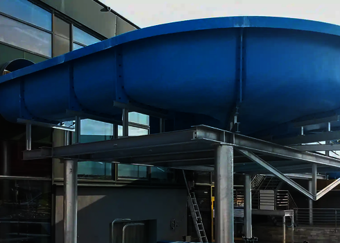 Blauer Wildwasserfluss beginnt an einer Glasfassade und ist auf einem Stahlgerüst montiert.