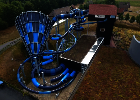 Luftbild des Cyclone in Blau mit verschlungenen Röhrenrutschen neben einem Flachdachgebäude.