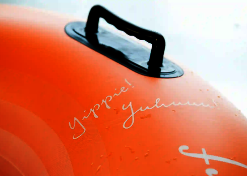 Nahaufnahme eines orangefarbenen Rutschreifens mit Griff und Schriftzug „Yippie! Juhuuu!“.