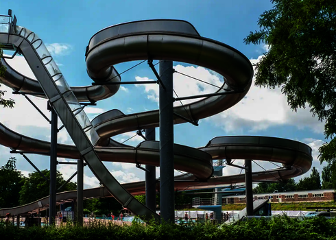 Mehrere ineinander verschlungene Edelstahlrutschen neben einer steilen Freifallrutsche.