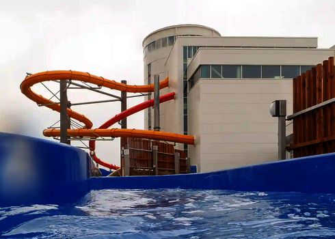 Blick aus einem blauen Wildwasserfluss auf eine gelbe und eine orangefarbene Wasserrutsche.