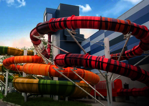 Bunte Röhren der Family Twister Rutsche winden sich in Rot, Orange, Gelb und Grün vor dem Startturm.