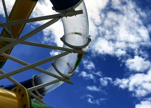 Durchsichtiger Rutschenabschnitt getragen von Stahlstützen und bunten Rutschen im Hintergrund.