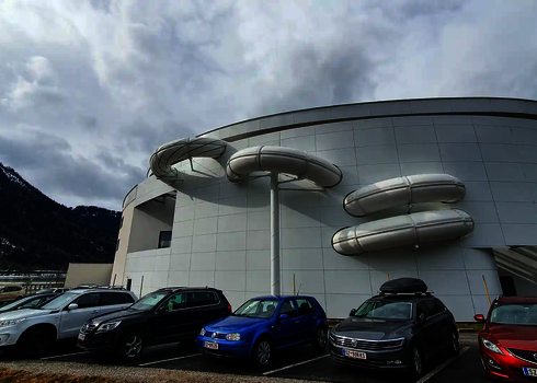  Gedämmte Röhrenrutsche verläuft mehrfach an der weißen Gebäudefassade eines Schwimmbads entlang.