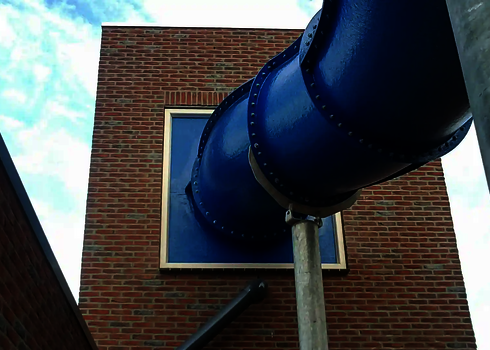 Eine blaue Wasserrutsche verlässt das Backsteingebäude durch eine markante Wandöffnung.