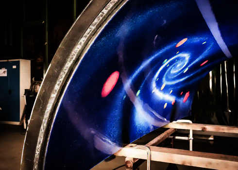 Lackiertes Rutschenmodul mit Galaxie-Motiv und Planeten unter UV-Licht in der Werkhalle.