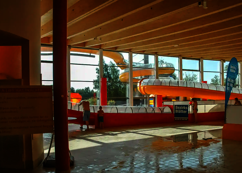 Schwimmbad mit Holzdecke und zwei Wasserrutschen in rot und gelb.