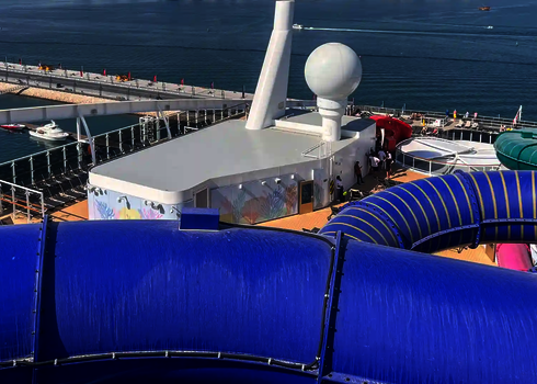 Blick von einem Kreuzfahrtschiff auf eine blaue Wasserrutsche, im Hintergrund der Ozean.