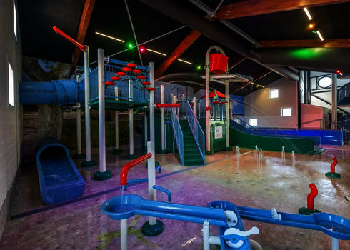 Kinderbereich in einem Hallenbad mit farbenfrohen Wasserrutschen und Spielgeräten. 