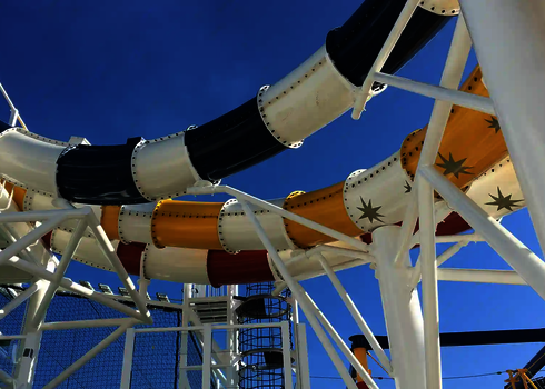 Wasserrutschen in mehreren Farben winden sich durch ein weißes Traggerüst an Deck.