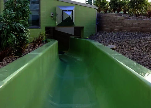 Grüner Wildwasserfluss verläuft vom Innen- in den Außenbereich durch eine Öffnung im Gebäude.