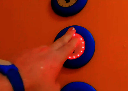 Finger drückt auf leuchtenden Auswahlknopf mit rotem LED-Ring an der Rutschenwand.