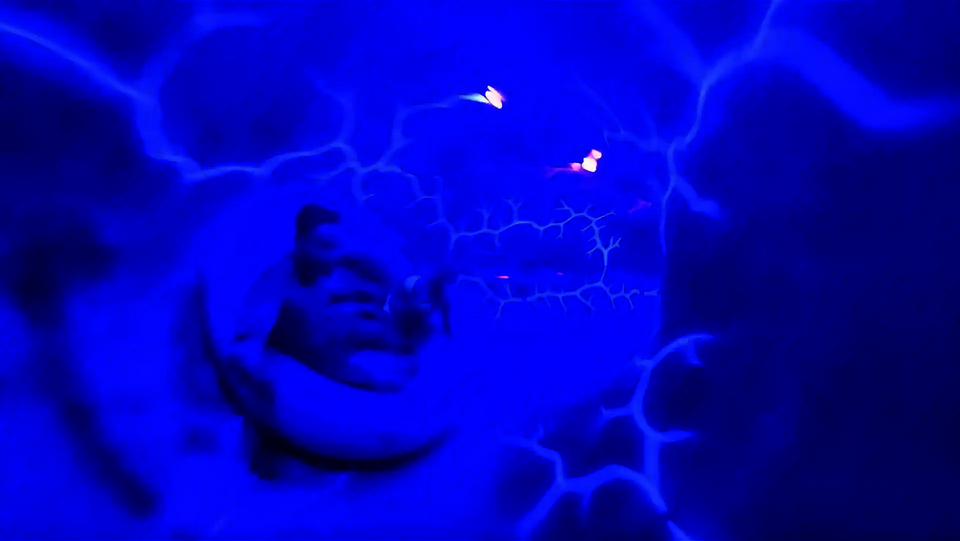 Rutschende Person in einer Röhre mit blauen UV-Blitzen an den Wänden.