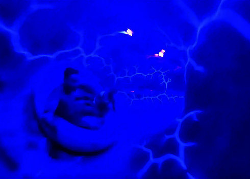 Rutschende Person in einer Röhre mit blauen UV-Blitzen an den Wänden.
