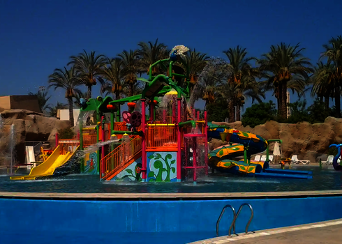 Farbenfroher Kinderbereich in einem Wasserpark in tropischer Umgebung mit Palmen.