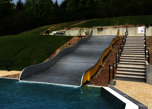 Eine Breitwellenrutsche mit gelben Seitenwänden, die einen grünen Hang hinabläuft.