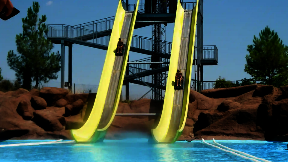 Felsige Umgebung hinter einer Aqua Shuttle Wasserrutsche mit zwei parallel laufenden Bahnen und rutschenden Personen.