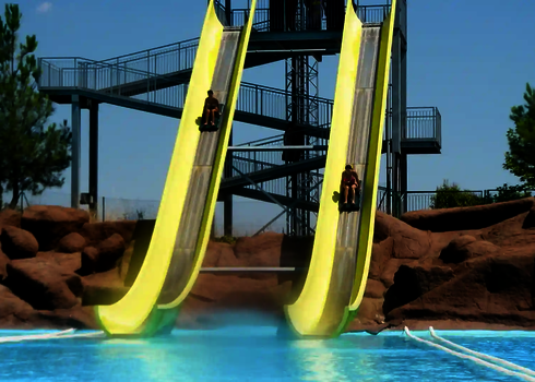 Felsige Umgebung hinter einer Aqua Shuttle Wasserrutsche mit zwei parallel laufenden Bahnen und rutschenden Personen.