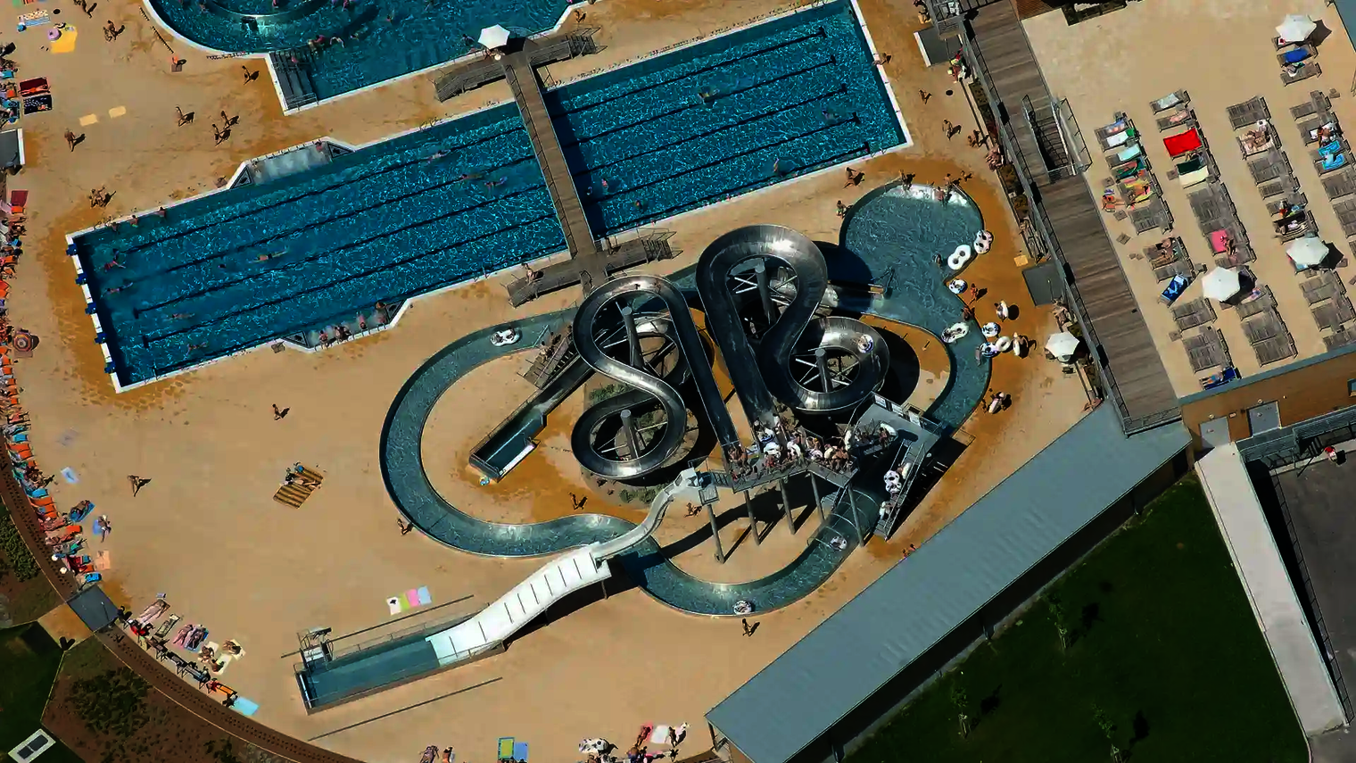 Luftaufnahme des Wasserparks mit einer Lazy River Rutsche, weiteren Edelstahl-Wasserrutschen und Schwimmbecken.