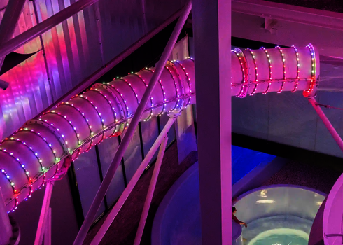 Blick von oben auf eine Röhre mit pinkfarbenen LED-Lichterketten im Hallenbad.