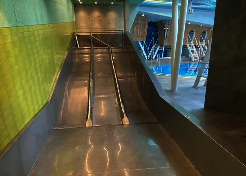 Trio-Slide im Innenbereich, daneben Schwimmbecken mit Sprungtürmen sichtbar.